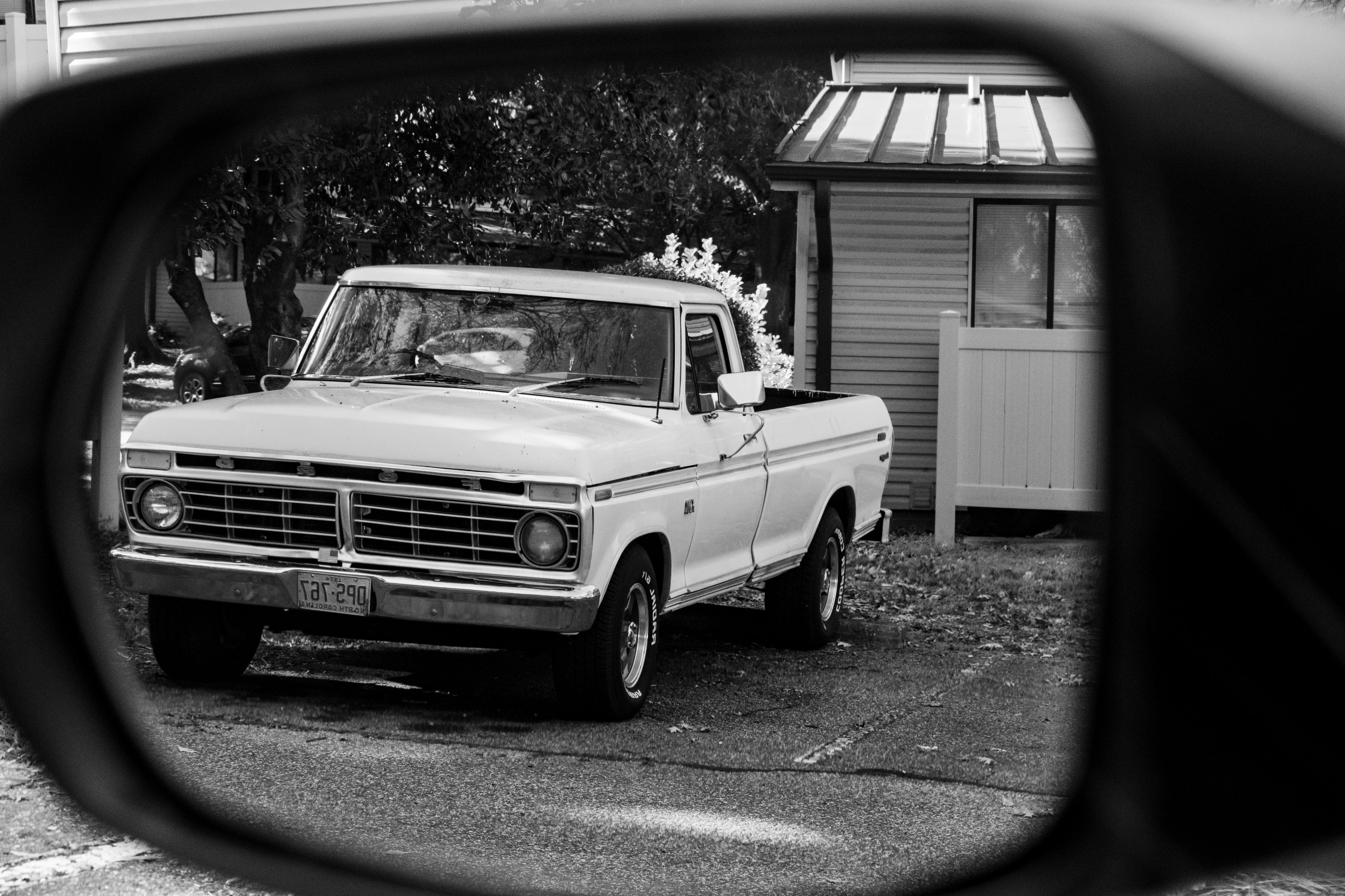 A black and white photo of a old Ford pick-up truck taken through the outside rear view mirror of my car.